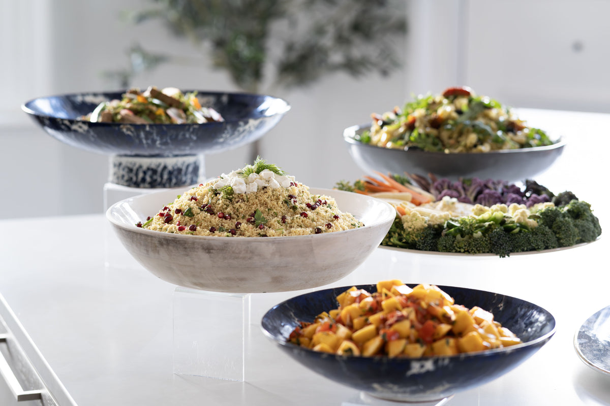 A styled dining table display featuring several ceramic bowls and platters holding prepared foods.