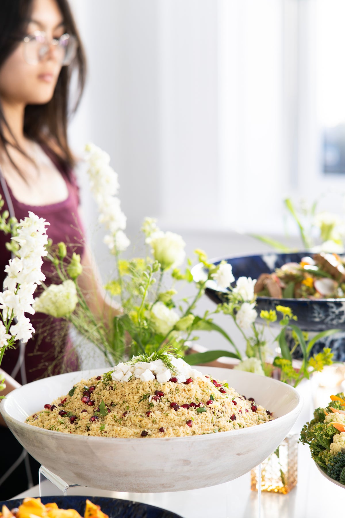 A large white bowl filled with cooked couscous or rice salad garnished with herbs and red berries.