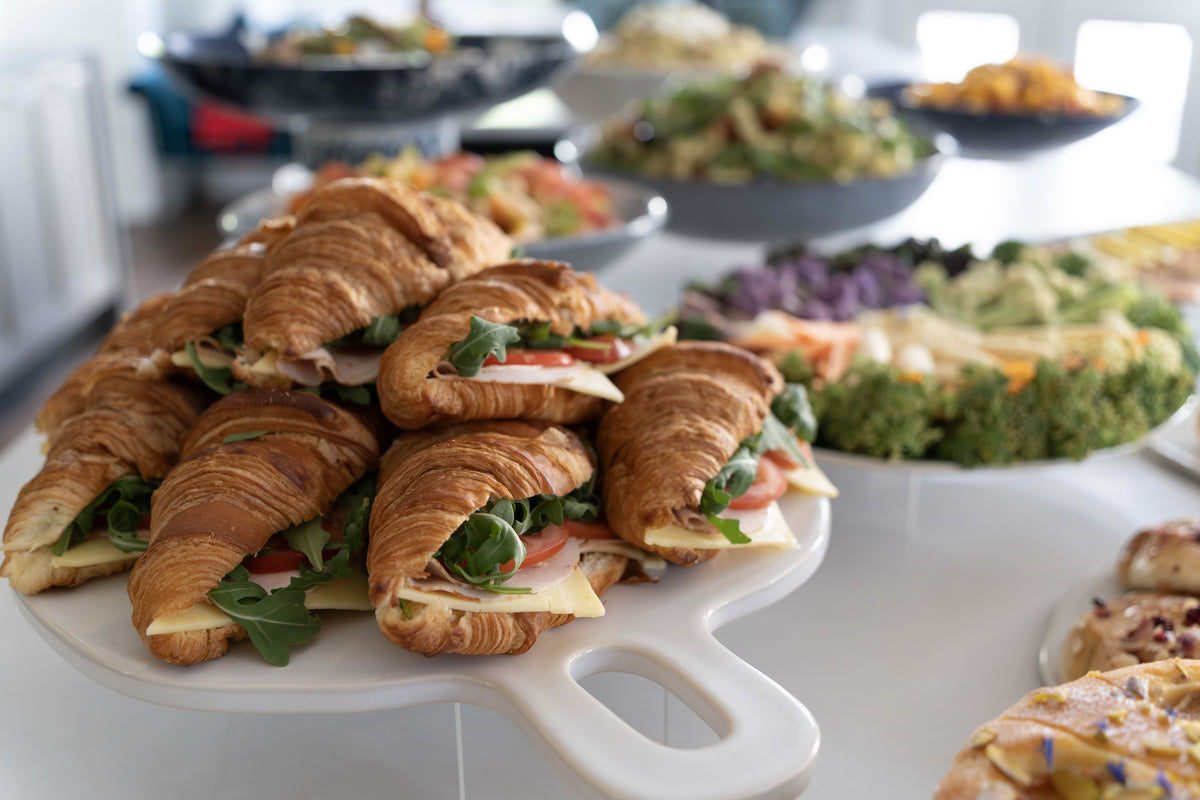 A white serving platter holding several croissant sandwiches filled with cheese, tomato, and greens.